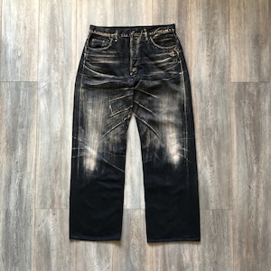 Puede incluir: Vaqueros de mezclilla de lavado oscuro con un dise&ntilde;o desgastado y descolorido. Los vaqueros tienen un dise&ntilde;o cl&aacute;sico de cinco bolsillos y un corte de pierna recta. La mezclilla tiene una apariencia desgastada con &aacute;reas m&aacute;s claras y marcas de desgaste visibles.