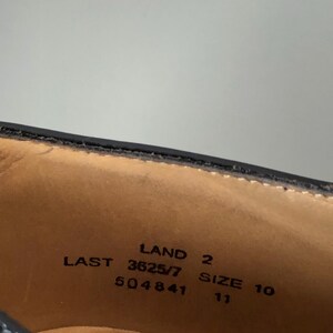 May include: Close-up of the inside of a black leather shoe. The shoe's interior is tan with black text that reads "LAND 2", "LAST 3625/7", "SIZE 10", and "504841". The size is also listed as 11.