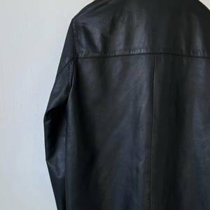 May include: A black leather jacket featuring a classic collar, long sleeves, and a horizontal back yoke seam. The garment displays a smooth, matte texture with visible stitching along the seams and a straight hemline, presented from a rear view.