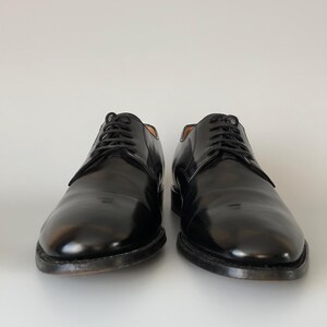 May include: A pair of black leather dress shoes with laces, presented on a white backdrop. The shoes have a polished, glossy finish and a classic design. The soles are dark. Suitable for formal events.