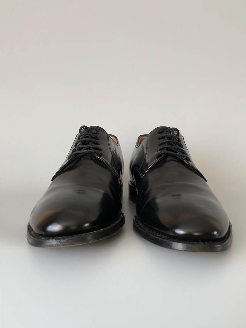 May include: A pair of black leather dress shoes with laces, presented on a white backdrop. The shoes have a polished, glossy finish and a classic design. The soles are dark. Suitable for formal events.
