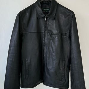 May include: A black jacket with a full-length front zipper, a standard collar, and long sleeves. The jacket features two lower side pockets and one horizontal chest pocket. The interior label displays the brand name Springfield in white text.