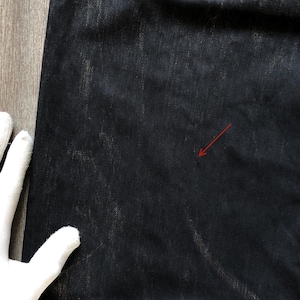 Puede incluir: Primer plano de unos vaqueros de mezclilla de lavado oscuro. Los vaqueros tienen un aspecto descolorido y desgastado con zonas m&aacute;s claras y un bolsillo trasero visible. La tela muestra sutiles patrones de desgaste, lo que sugiere una est&eacute;tica vintage o usada.
