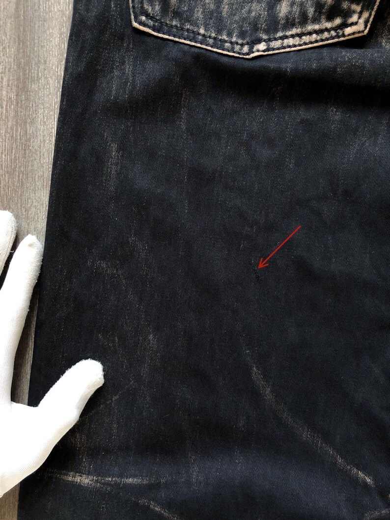 Puede incluir: Primer plano de unos vaqueros de mezclilla de lavado oscuro. Los vaqueros tienen un aspecto descolorido y desgastado con zonas m&aacute;s claras y un bolsillo trasero visible. La tela muestra sutiles patrones de desgaste, lo que sugiere una est&eacute;tica vintage o usada.