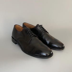 May include: A pair of black leather dress shoes with laces. The shoes have a glossy finish and a classic design, suitable for formal occasions. The shoes are displayed on a white surface.