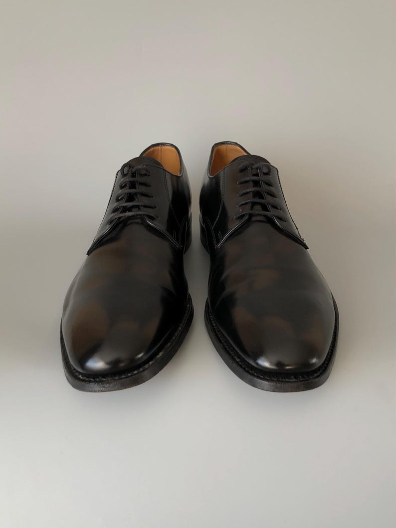 May include: Two black leather dress shoes with a high-shine finish and a traditional lace-up closure. The shoes have a rounded toe and a dark sole. The image shows the shoes against a plain background, suitable for formal wear.