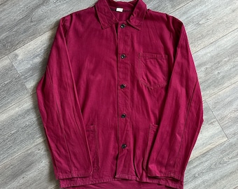 May include: A long-sleeved, button-down jacket in a deep magenta color. This garment features a classic collar, a single chest pocket on the left side, and two additional pockets at the lower front. The jacket is secured with five dark buttons.