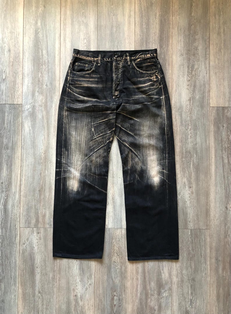 Puede incluir: Vaqueros de mezclilla de lavado oscuro con una apariencia descolorida y desgastada. Los vaqueros tienen bragueta con botones y un estilo cl&aacute;sico de cinco bolsillos. La mezclilla tiene un aspecto desgastado y vintage con &aacute;reas claras y decoloraci&oacute;n vertical.