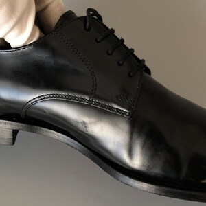 May include: A black leather dress shoe with a polished finish. The shoe has a lace-up design and a low heel. Stitching is visible along the seams. The shoe is a classic style, suitable for formal events. The shoe's length is approximately 28 cm.