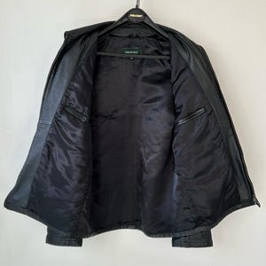 May include: A black leather jacket with a smooth black interior lining, a front zipper closure, and two interior chest pockets. The jacket features a label at the neck with the text Springfield, and it is displayed on a black plastic hanger.