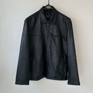 May include: A black leather jacket featuring a classic collar, a full-length front zipper closure, and two lower side pockets. The garment includes a horizontal seam across the chest and a small chest pocket, with a Springfield brand label inside.