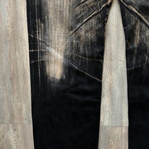 Puede incluir: Vaqueros negros de mezclilla con un dise&ntilde;o descolorido y desgastado. Los vaqueros tienen un corte de pierna recta y un efecto degradado, pasando del negro a una apariencia m&aacute;s clara y desgastada. La tela muestra patrones de desgaste visibles.