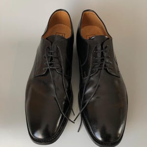 May include: A pair of black leather dress shoes with laces. The shoes have a glossy finish and a classic design, suitable for formal occasions. The soles are dark, and the interior is a light brown colour.