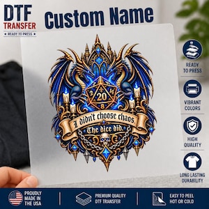 May include: A DTF transfer sheet featuring a graphic of two blue dragons flanking a 20-sided die. Below the die is a banner with the text 'I didn't choose chaos. The dice did.' and a skull. The design includes candles and gothic architectural elements.