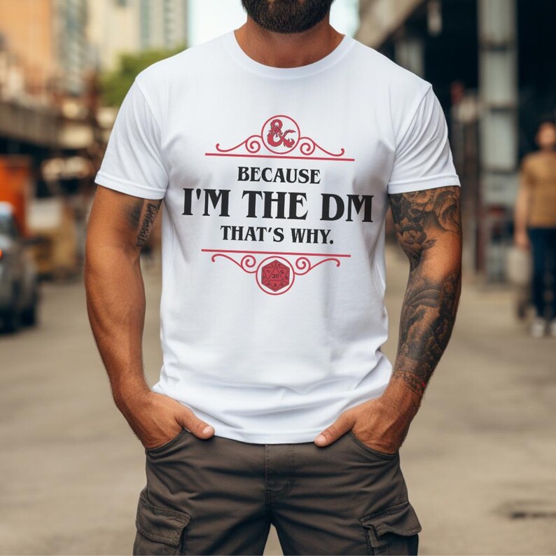 Puede incluir: Camiseta blanca con el texto "BECAUSE I'M THE DM THAT'S WHY." en negro y rojo. La camiseta presenta un logotipo de Dungeons & Dragons. La camiseta es de cuello redondo y manga corta.