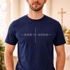 May include: Navy blue crew neck t-shirt with the text "-GOD IS GOOD-" in white. The text is centered on the chest, with a vertical line intersecting the text. The shirt is made of a soft material.