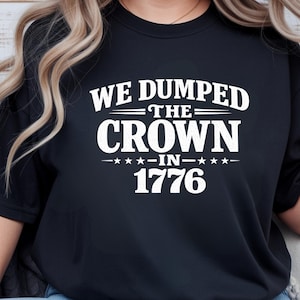 May include: Black crew neck sweatshirt with the white text "WE DUMPED THE CROWN -IN- 1776". The text is centered on the front of the shirt. The sweatshirt is a solid black color.