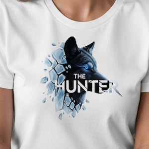 May include: White t-shirt featuring a black wolf graphic with blue eyes and the text "THE HUNTER". The wolf design appears to be breaking through a shattered ice effect.