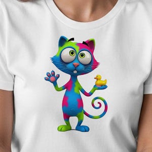 Op de afbeelding: Wit T-shirt met een kleurrijke cartoonkat die een gele badeend vasthoudt. De kat heeft een blauw gezicht, groene ogen en een roze en groene kop. Zijn lichaam is een mix van blauw, roze en groen.