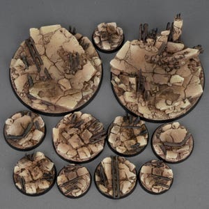Puede incluir: Una colección de diez bases circulares en miniatura con un diseño de terreno de piedra agrietada en tonos beige y bronceado, acentuado con escombros de color marrón oscuro y elementos de madera astillada sobre superficies rocosas.
