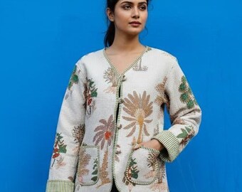 May include: Cream-colored jacket with a floral pattern, featuring a V-neck, pockets, and green striped trim. The jacket is worn over blue jeans against a bright blue background. The floral design includes shades of brown, green, and red.
