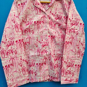 Może przedstawiać: R&oacute;żowa i biała koszula do piżamy z powtarzającym się wzorem pionowych pask&oacute;w oraz motyw&oacute;w architektonicznych i palm. Koszula z długim rękawem ma kołnierzyk, kieszeń na piersi i zapięcia na guziki.