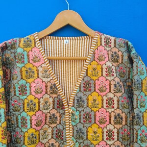 May include: A colorful, quilted jacket with a floral pattern in shades of yellow, pink, blue, and gray. The jacket has a V-neck and is lined with a striped fabric. The size "L" is visible on the hanger.