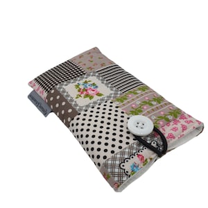 Könnte beinhalten: Eine Handyhülle aus Patchwork-Stoff mit Blumenmuster, schwarzen Punkten und einem weißen Knopfverschluss. Die Hülle hat ein braunes und weißes Gummiband.