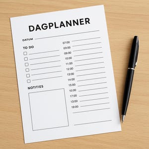 Op de afbeelding: Een witte "DAGPLANNER" notitieblok en een zwarte pen op een lichtbruin houten oppervlak. Het notitieblok bevat secties voor "DATUM", "TO DO" en "NOTITIES", met tijdsperioden van 07:00 tot 19:00 uur. De pen is zwart met zilveren details.