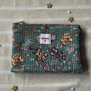 Op de afbeelding: Een gewatteerde, turquoise etui met een bloemenpatroon in bruin, geel en bordeaux. De etui heeft een gouden rits en een klein wit label met "BÉCOTE" en een rood hart.