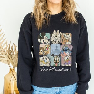 May include: Black sweatshirt featuring a colorful graphic of Disney characters in square frames. The design includes Mickey Mouse, Minnie Mouse, Donald Duck, and other beloved characters. The words "Walt Disney World" are printed below the graphic.
