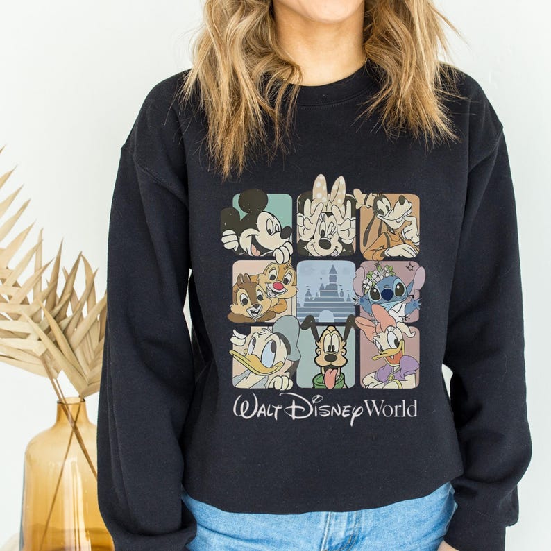 May include: Black sweatshirt featuring a colorful graphic of Disney characters in square frames. The design includes Mickey Mouse, Minnie Mouse, Donald Duck, and other beloved characters. The words "Walt Disney World" are printed below the graphic.