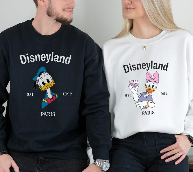 Pode incluir: Camisolas Disneyland azuis marinho e brancas. A camisola azul marinho apresenta o Pato Donald, e a camisola branca apresenta a Margarida. Ambas as camisolas t&ecirc;m o log&oacute;tipo da Disneyland, o texto "est. 1992 PARIS".