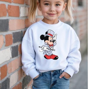 K&ouml;nnte beinhalten: Wei&szlig;es Sweatshirt mit einem Cartoon-Motiv von Mickey Mouse als Zauberer. Mickey tr&auml;gt einen grauen Anzug, rote Schuhe und einen Zylinder. Das Sweatshirt wird mit einer blauen Jeans kombiniert.