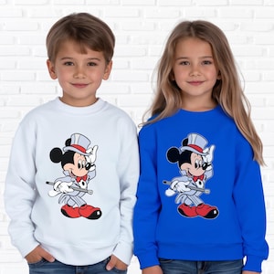 K&ouml;nnte beinhalten: Zwei Kinder tragen Sweatshirts. Eines ist wei&szlig;, das andere blau. Beide Sweatshirts zeigen ein Cartoon-Mickey-Mouse-Design in einem Smoking, Zylinder und roten Schuhen. Das Design beinhaltet einen Gehstock. Die Kinder l&auml;cheln.