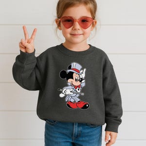 K&ouml;nnte beinhalten: Dunkelgraues Sweatshirt mit einem Cartoon-Mickey-Mouse-Magier-Outfit. Mickey tr&auml;gt einen Zylinder, eine rote Fliege und rote Schuhe. Das Sweatshirt hat einen Rundhalsausschnitt.