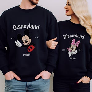 Pode incluir: Camisolas pretas a condizer com desenhos do Mickey e da Minnie. As camisolas apresentam o texto "Disneyland Paris", o ano "1992" e a palavra "est.". Mickey Mouse faz o sinal de paz.