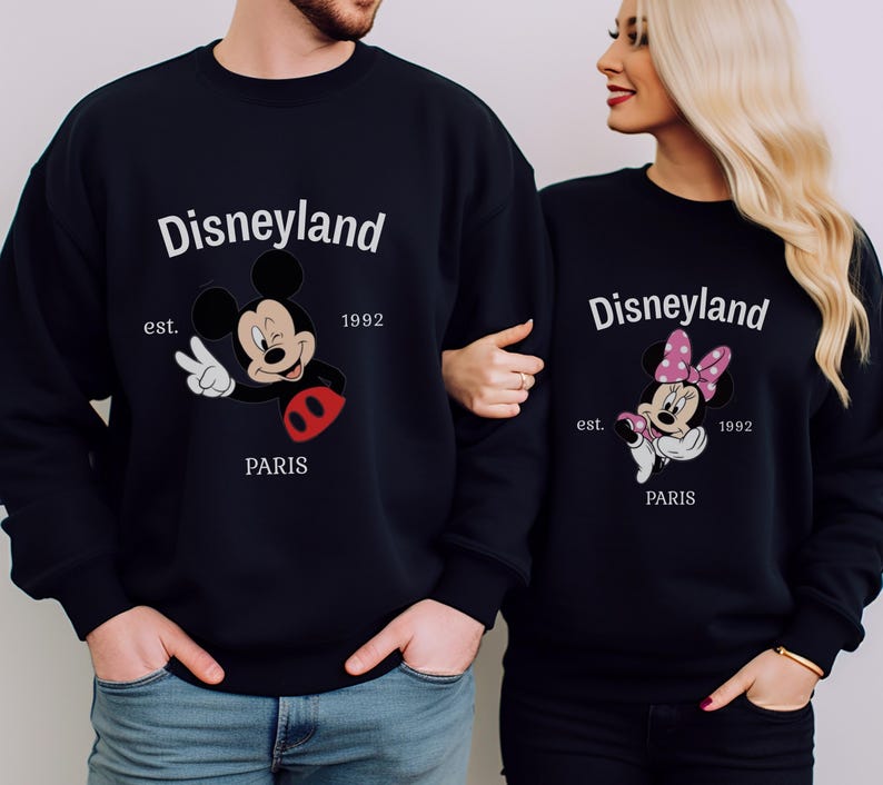 Pode incluir: Camisolas pretas a condizer com desenhos do Mickey e da Minnie. As camisolas apresentam o texto "Disneyland Paris", o ano "1992" e a palavra "est.". Mickey Mouse faz o sinal de paz.