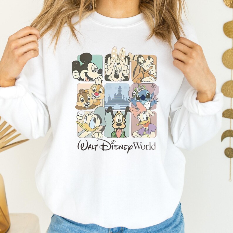 May include: White sweatshirt featuring a colorful grid of Disney characters, including Mickey Mouse, Minnie Mouse, and Goofy. The design includes Chip and Dale, a castle, Stitch, Donald Duck, Pluto, and Daisy Duck. The words "Walt Disney World" are printed below the grid.