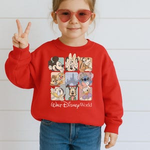 May include: A red sweatshirt featuring a grid of Disney characters, including Mickey Mouse, Minnie Mouse, and Donald Duck. The words "Walt Disney World" are printed below the grid. The sweatshirt is worn by a child.