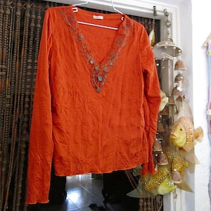 Puede incluir: Camiseta naranja de manga larga con cuello de cuentas y textura arrugada.