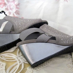 May include: A pair of grey wedge sandals with rhinestones. The sandals have a strap across the foot and an ankle strap.