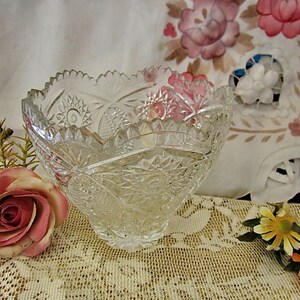 Peut inclure: Un bol en verre transparent avec un motif en verre taill&eacute;. Le bol est pos&eacute; sur une nappe en dentelle blanche avec des fleurs roses et jaunes.