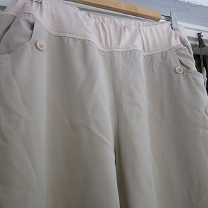May include: A pair of light beige trousers with a wide waistband and two pockets. The waistband has a contrasting light pink fabric trim.