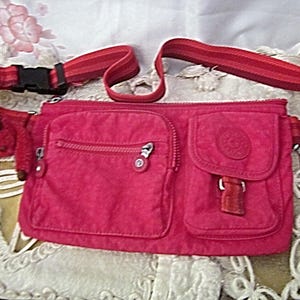 Peut inclure: Un sac banane rose vif avec plusieurs compartiments zippés et une poche à rabat. La sangle réglable et la boucle sont rouges. Un petit porte-clés singe est attaché sur le côté.