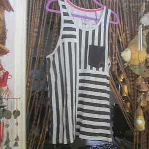 以下が含まれることがあります： グレーと白のストライプのタンクトップ、黒いポケット付き。タンクトップは紫色のハンガーに掛けられています。トップはピンクのトリムが付いた丸いネックラインです。