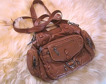 Hermoso bolso de mano o de hombro con múltiples bolsillos de cuero genuino suave en color marrón burdeos, con tachuelas y dos cierres con cremallera