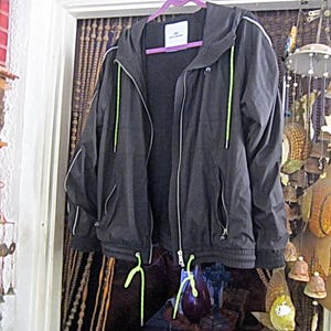 May include: A black hooded jacket with a zipper closure and green drawstrings. The jacket has white piping around the edges and a white label on the front.
