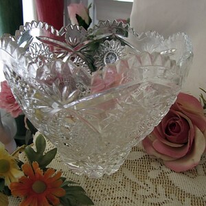 Peut inclure: Un bol en verre transparent avec un motif en verre taill&eacute;. Le bol est pos&eacute; sur une nappe en dentelle avec des roses roses et d'autres fleurs.