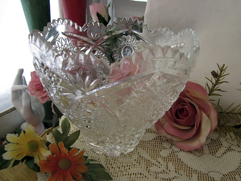 Peut inclure: Un bol en verre transparent avec un motif en verre taill&eacute;. Le bol est pos&eacute; sur une nappe en dentelle avec des roses roses et d'autres fleurs.